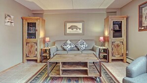 A living room with a sofa, two side tables with lamps, a coffee table, and two wooden cabinets with bookshelves. - Spacious Condo in the Heart of Center Village - Pet Friendly - VS367 by Redawning (Copper Mountain)