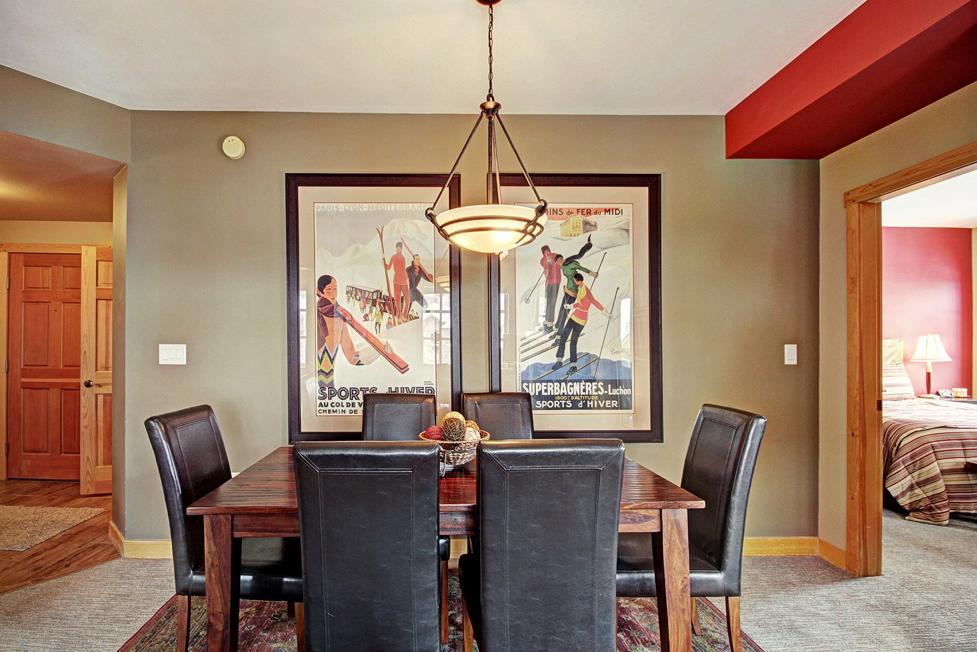 A dining area with a wooden table and black chairs, a chandelier, and two framed posters on the wall.