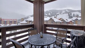 A balcony with a round table and chairs, overlooking a snowy mountain town.
