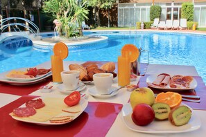 Ein Frühstückstisch mit Croissants, Gebäck, Obst und Kaffee am Pool.