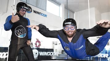 Deux personnes vêtues de combinaisons de course ornées de logos, debout dans une pièce dotée d’une grande fenêtre et d’une enseigne sur laquelle on peut lire « WINDOOR ».