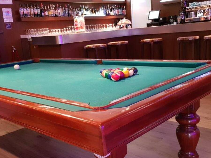 Una mesa de billar con bolas, una zona de bar con botellas y taburetes.