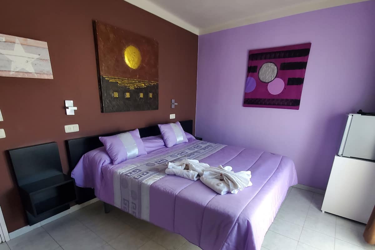 A bedroom with a bed, a wall clock, and a refrigerator.