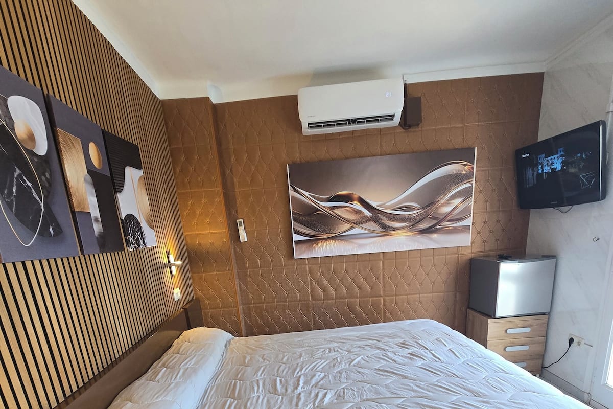A hotel room with a bed, a mounted television, and a wall-mounted air conditioner.