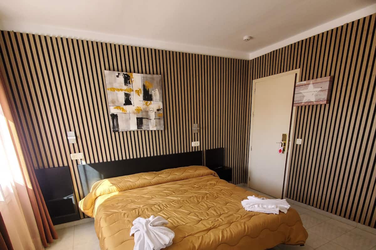 A hotel room with a large bed, a flat-screen TV, a bedside table, and a wall-mounted artwork.