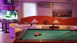 A pool table with balls, a television displaying a sports game, a sofa, and a cityscape painting. - Hotel Ampuria Inn (Castello d'Empuries)