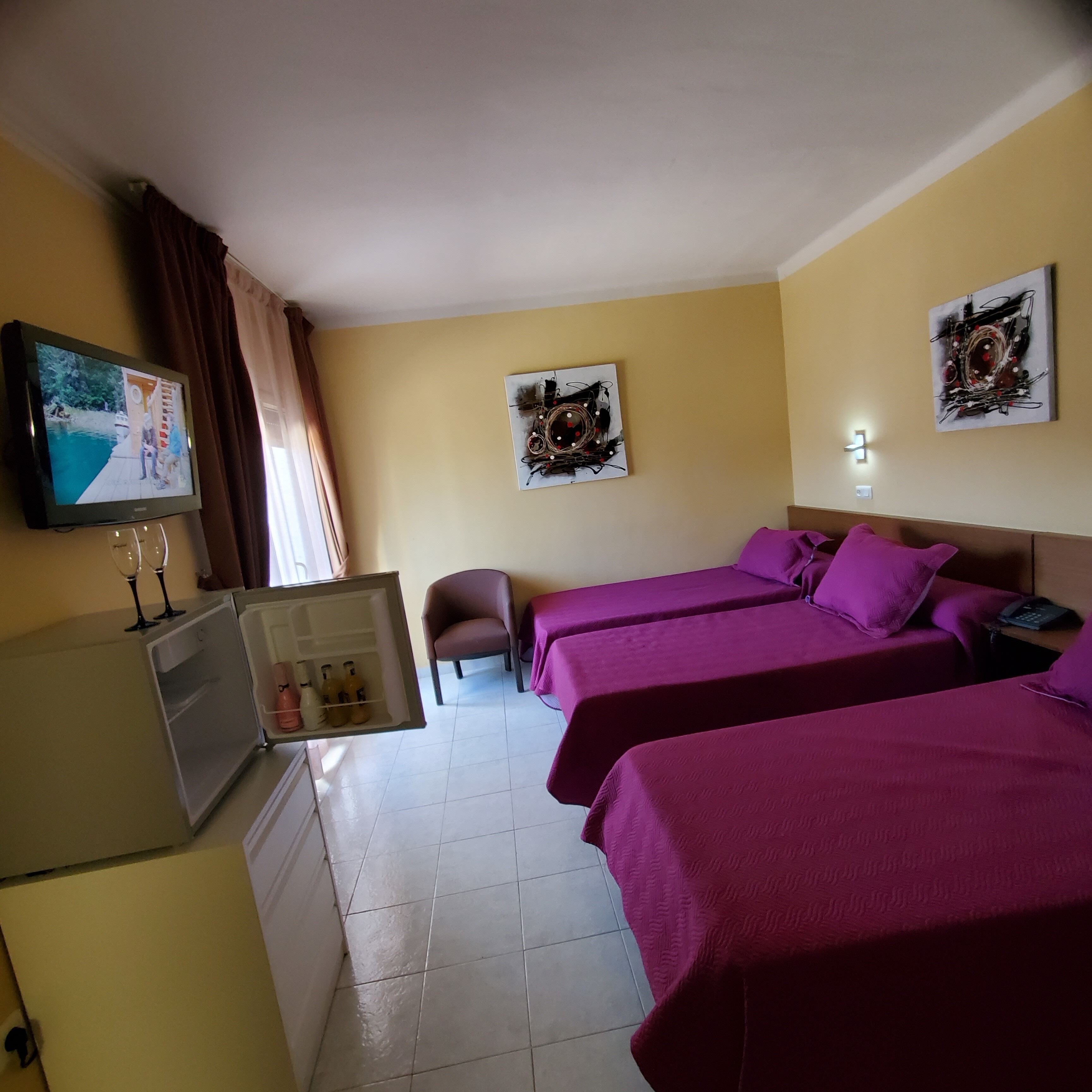 A hotel room with two beds, a small desk, a refrigerator, and a television on the wall.