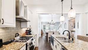 A modern kitchen with white cabinetry, granite countertops, stainless steel appliances, and a central island with a sink. - 'Seas the Day' in WaterColor Beach 5 Bdrm/Slps 10| Steps to Dragonfly Pool! (Santa Rosa Beach)