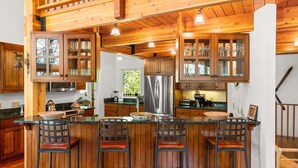 A kitchen with wooden cabinets, a stainless steel refrigerator, and a bar area with stools. - RMR: The Village House in Teton Village (Teton Village)