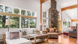 A spacious living room with a stone fireplace, large windows, and a high ceiling. - RMR: The Village House in Teton Village (Teton Village)
