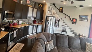 A modern living room with a dark brown sectional sofa, a kitchen area with stainless steel appliances, and a staircase leading to an upper level. - Country get away in Waxahachie, TX on 10 acres Shared with The Yurt in the Woods (Waxahachie)