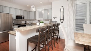 Una cocina moderna con una isla central, taburetes de bar, un refrigerador de acero inoxidable y un microondas.