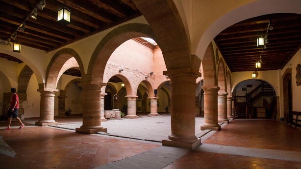 Une cour spacieuse, agrémentée de nombreuses arcades et de colonnes, avec un sol carrelé et un plafond en bois.