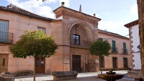 Une cour avec une fontaine, des bancs en pierre et un bâtiment doté d’un toit en tuiles et d’une entrée en arc de cercle.