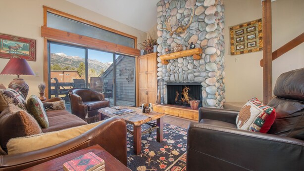 Un salon chaleureux avec une cheminée en pierre, des meubles en cuir et une grande fenêtre donnant sur les montagnes.