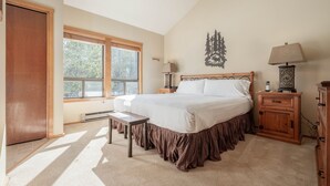 Une chambre à coucher avec un grand lit, une table de chevet, une commode, une fen être avec des stores et un élément décoratif mural.