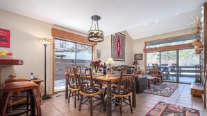 Un vaste espace dédié à la salle à manger, avec une table et des chaises en bois, un lustre, et une vue sur une terrasse extérieure accessible par de grandes portes coulissantes en verre.