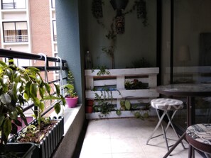 Un balcón con plantas en macetas, un banco blanco y una pequeña mesa.