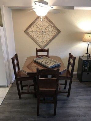 Un coin repas avec une table en bois et quatre chaises, un élément décoratif mural au-dessus de la table et une lampe sur une table d’appoint.