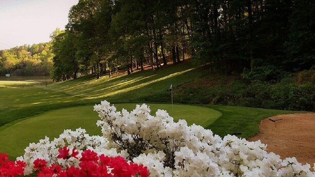 Ein Golfplatz mit gepflegter Spielbahn, Sandbunkern und einem Clubhaus.