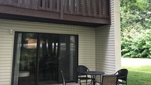 Ein zweigeschossiges Haus mit einem Balkon, einer Schiebetür und einer Terrasse mit Tisch und Stühlen.