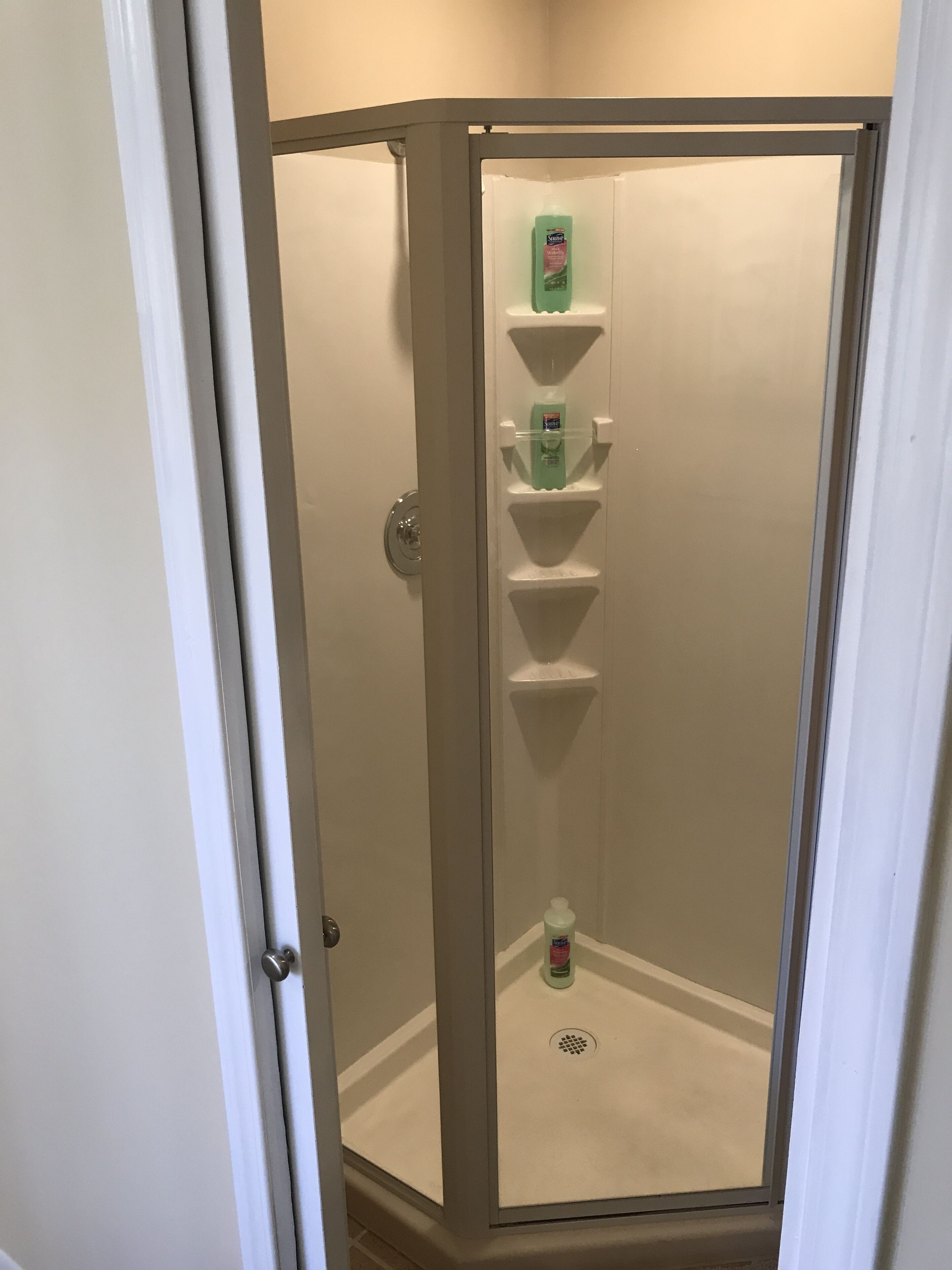 A walk-in shower with a glass door, a white tiled floor, and a shelf with toiletries.