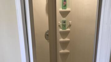 A walk-in shower with a glass door, a white tiled floor, and a shelf with toiletries.