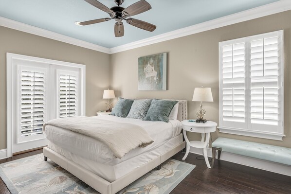 A bedroom with a bed, two bedside tables, a bench, a ceiling fan, and two windows with shutters. - 2 Golf Carts ~ Golf Course View ~ Community Pool (Miramar Beach)