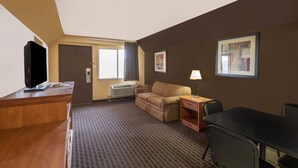 Een hotelkamer met een houten bureau, een televisie, een sofa, een klein tafeltje met een lamp en een lijstje aan de muur.