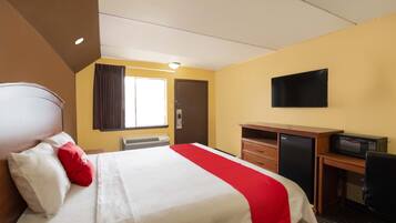 A hotel room with a bed, a desk, a television, and a window with curtains.
