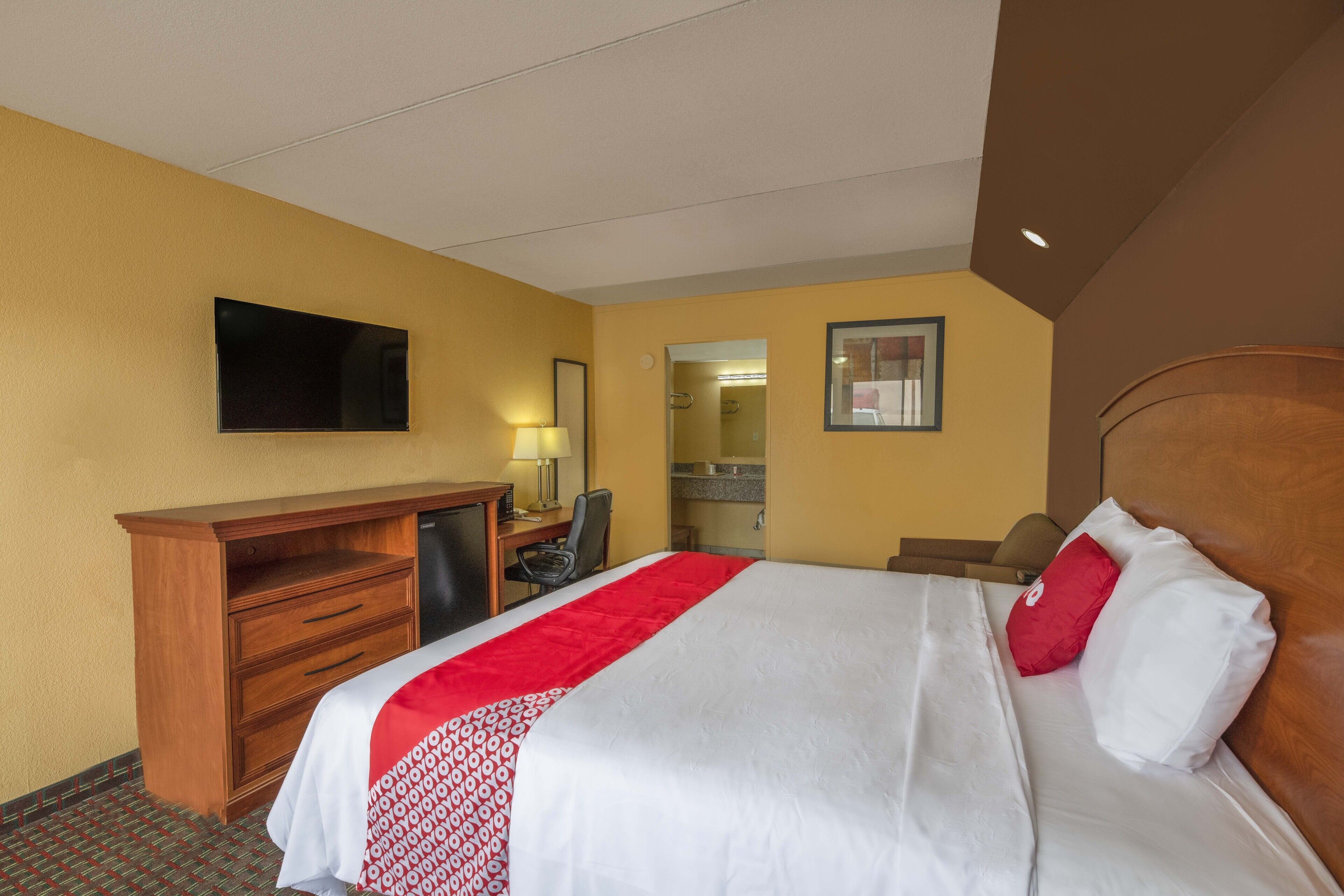 Een hotelkamer met een bed, bureau, stoel, televisie en spiegel.