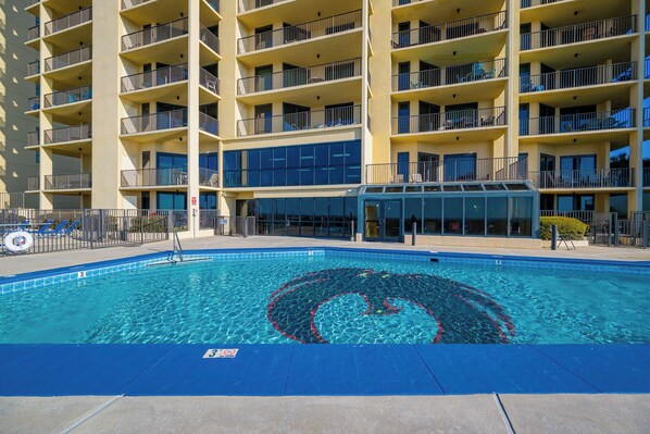 A swimming pool with a circular design, surrounded by a building with multiple balconies and a glass facade.
