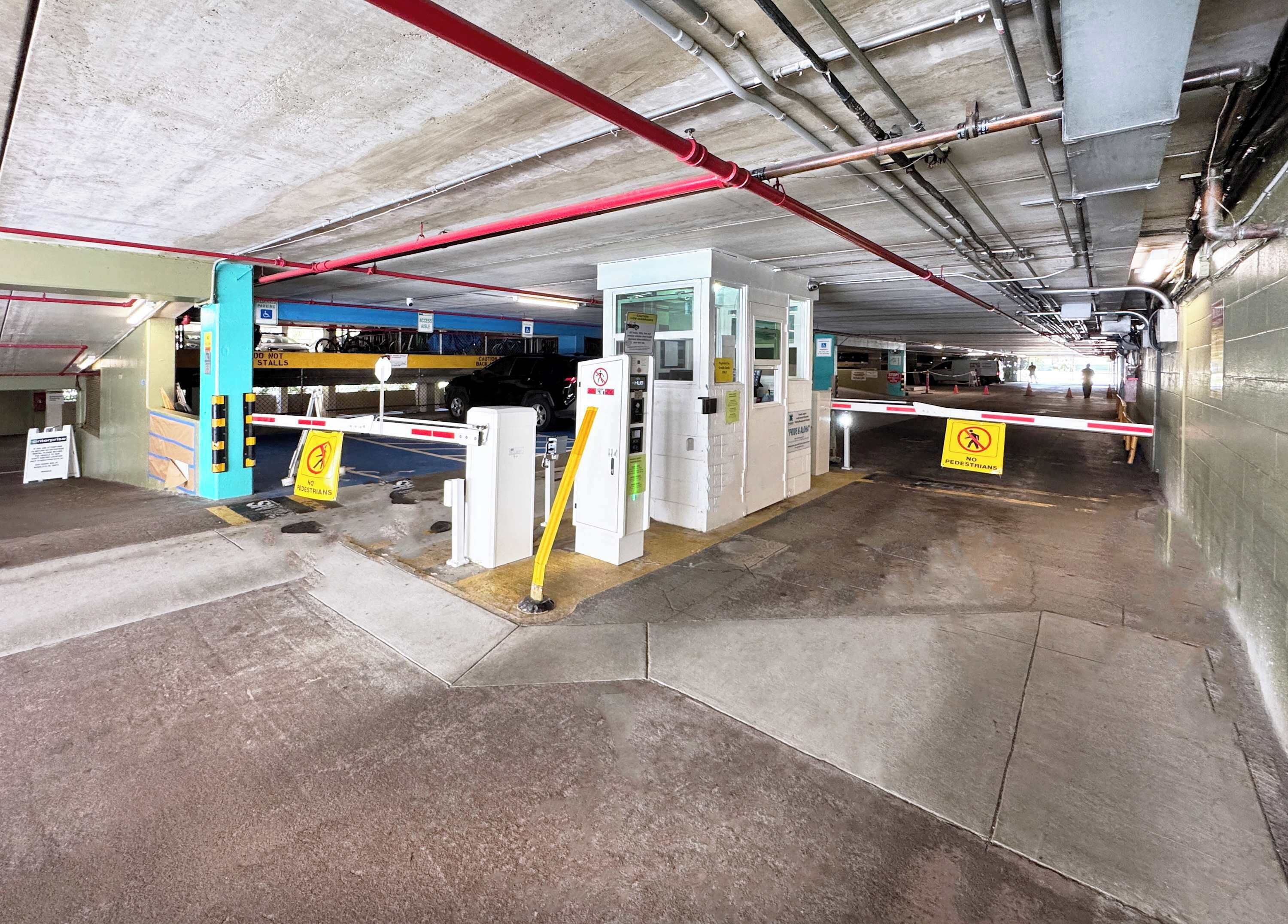 An underground parking garage with concrete floors, metal barriers, and a pedestrian crossing.