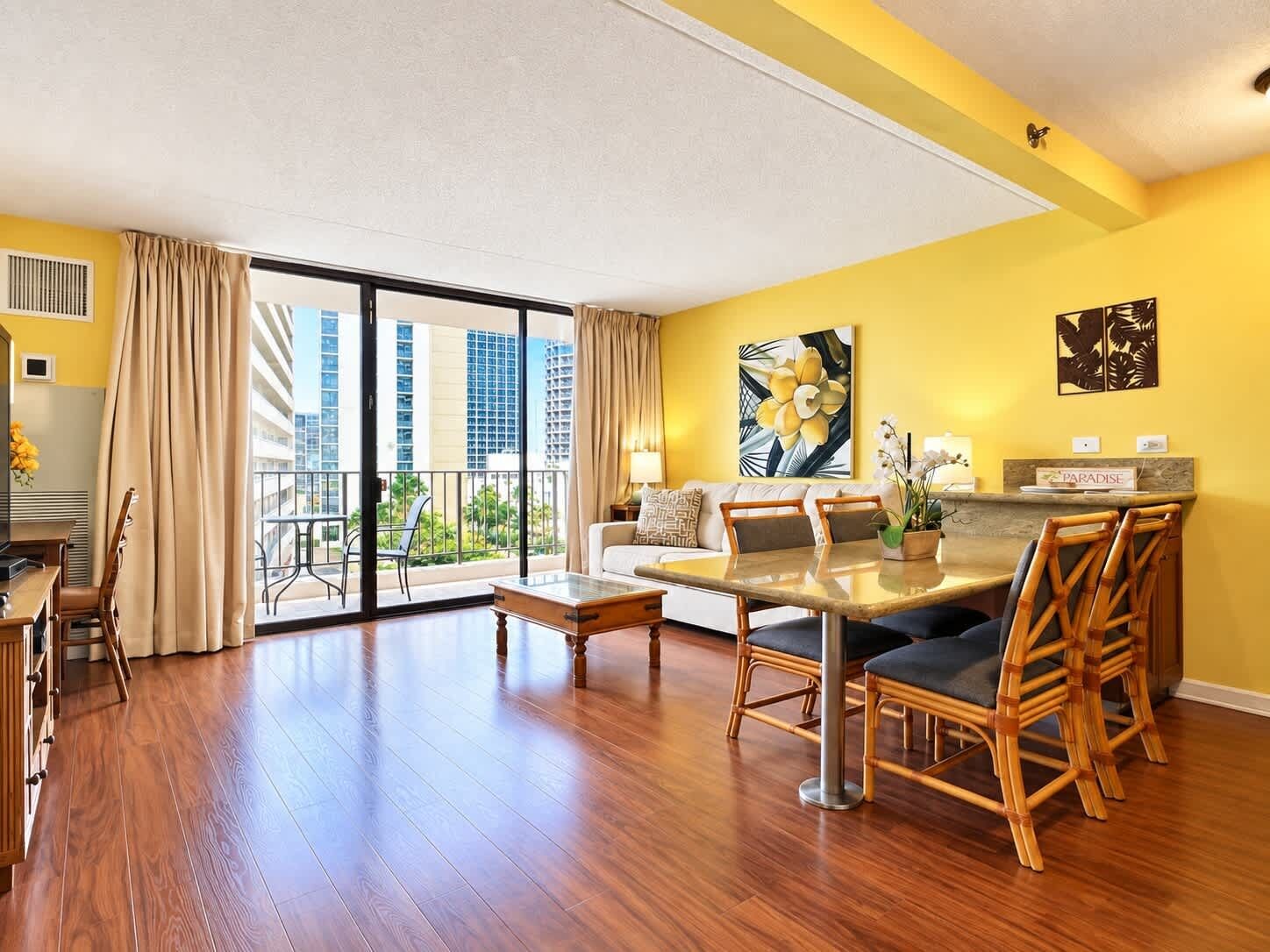Ein geräumiges Wohnzimmer mit Balkon, einem Essbereich und Blick auf hohe Gebäude.