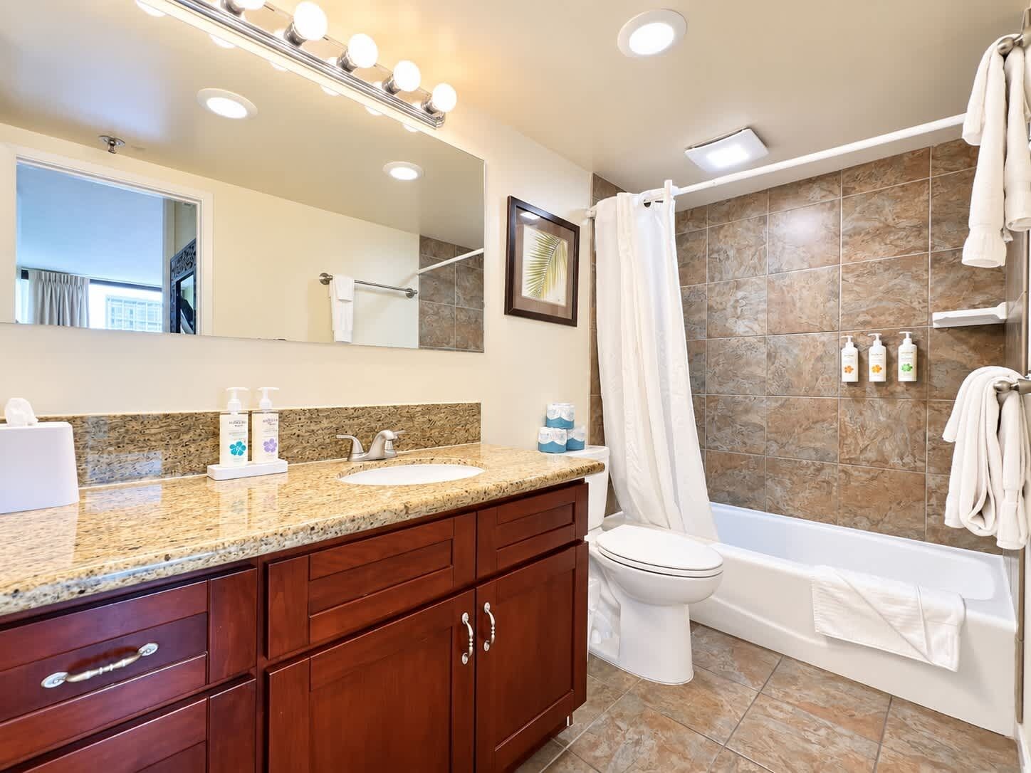 A bathroom with a vanity, sink, mirror, shower, and toilet.