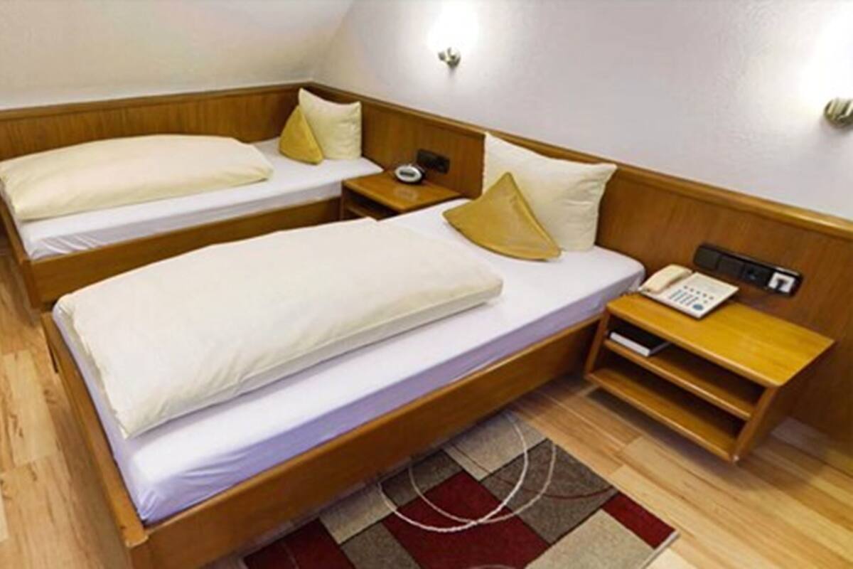 Ein Zimmer mit zwei Einzelbetten, jeweils mit einem Holzkopfende, einem Nachttisch mit Lampe und einer kleinen Ablage.