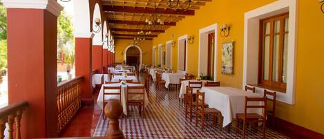A long corridor with tables and chairs, wooden railings, and a patterned floor.