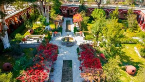 An aerial view of a courtyard with a central fountain, surrounded by red flowering plants and trees. - DM Hoteles Mossone Ica (Ica)
