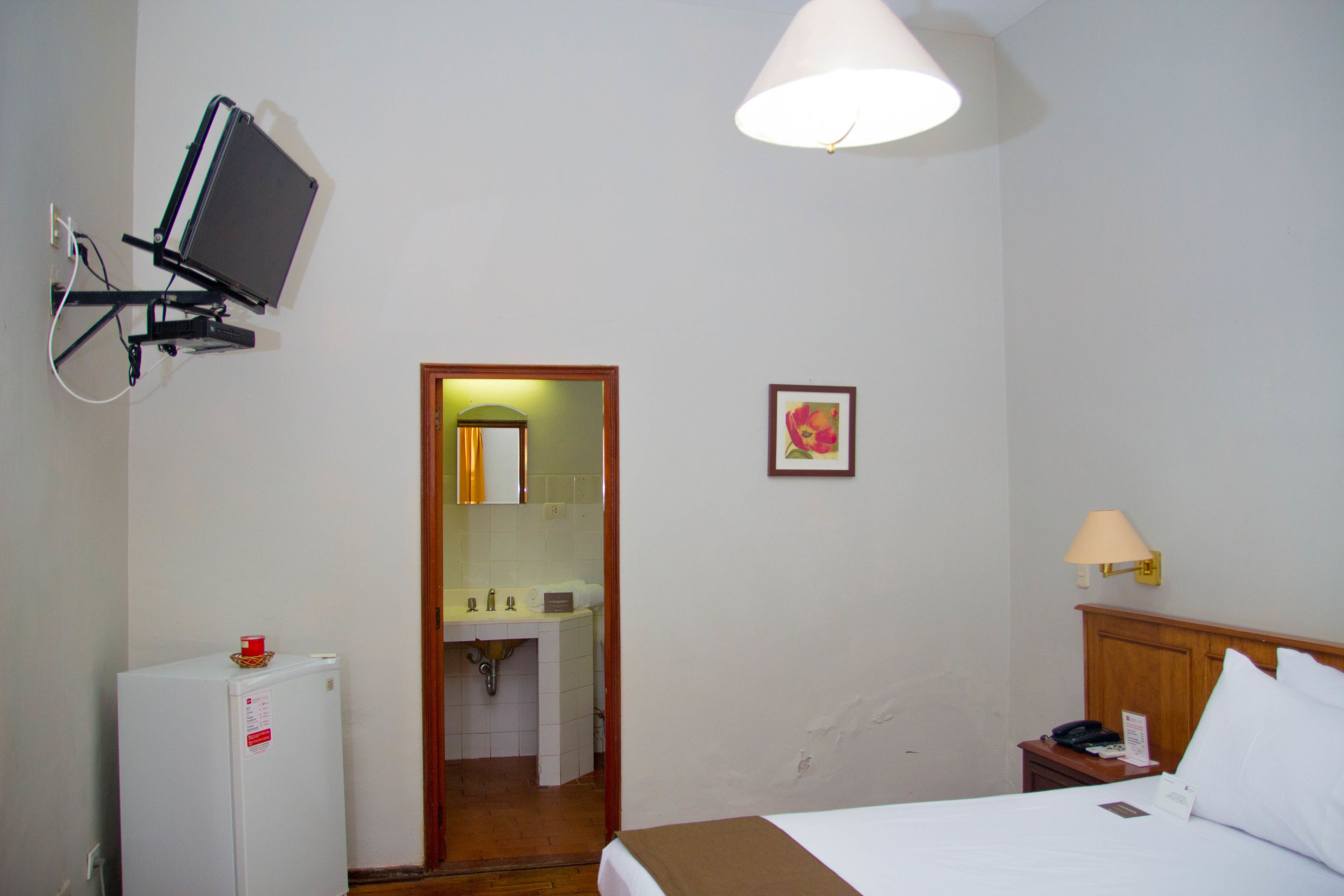 A hotel room with a bed, a desk, a lamp, a TV, and a small fridge.