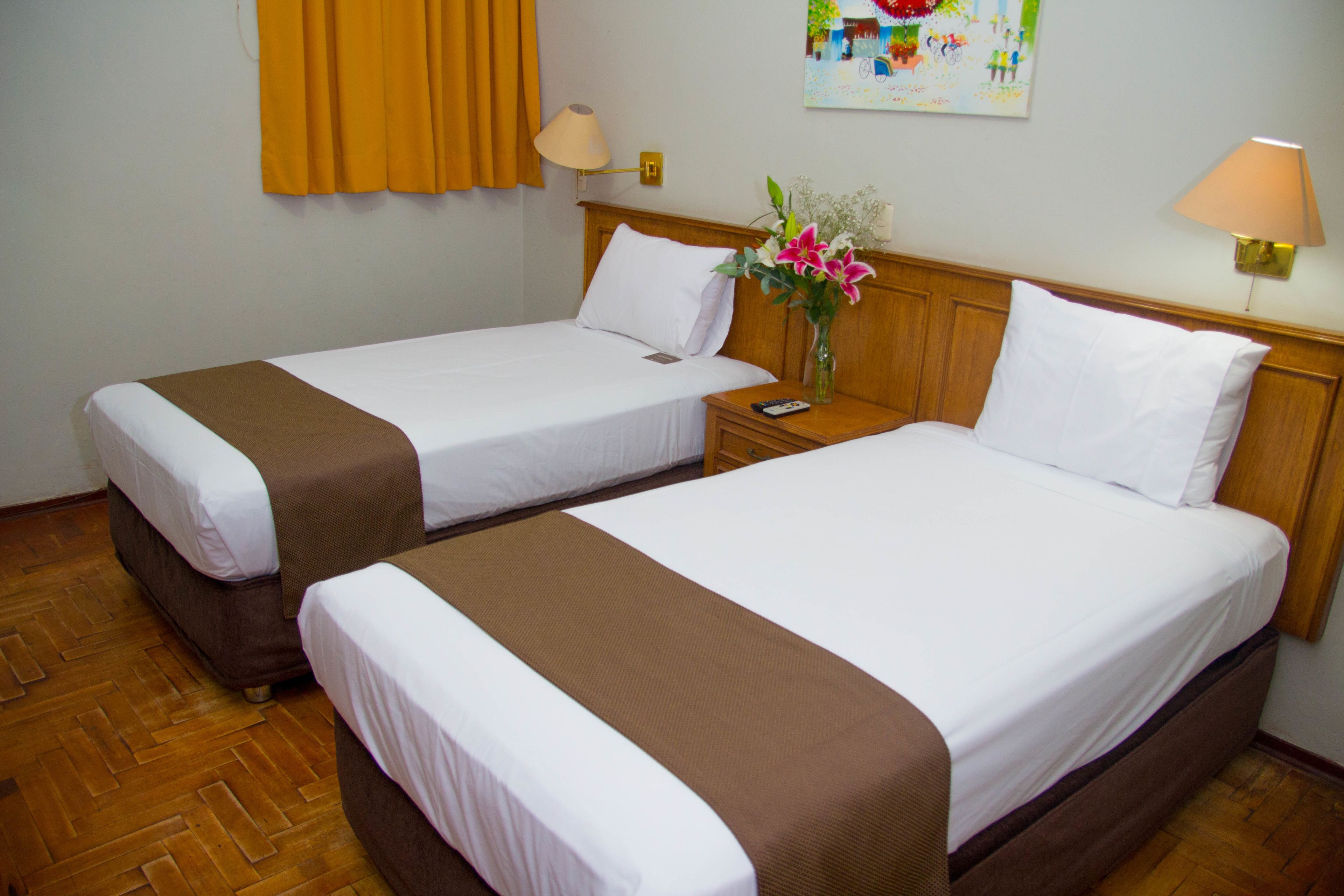 Two single beds with brown headboards, white linens, and a nightstand with a lamp between them.