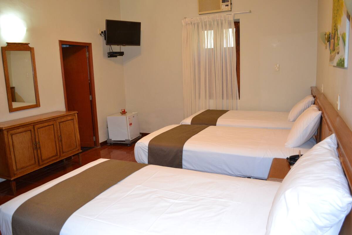 A hotel room with two beds, a wooden cabinet, a television, and a window with curtains.