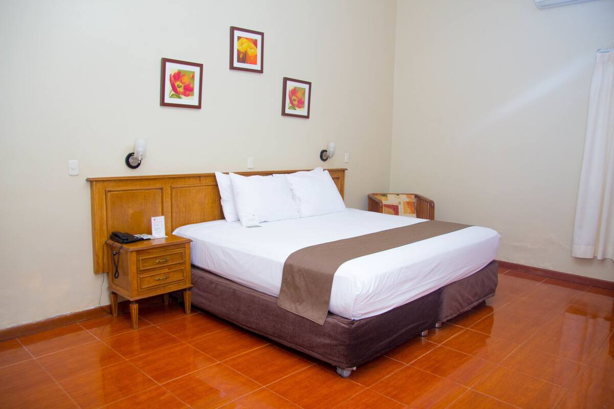 A hotel room with a large bed, wooden headboard, bedside tables, and wall-mounted lamps.