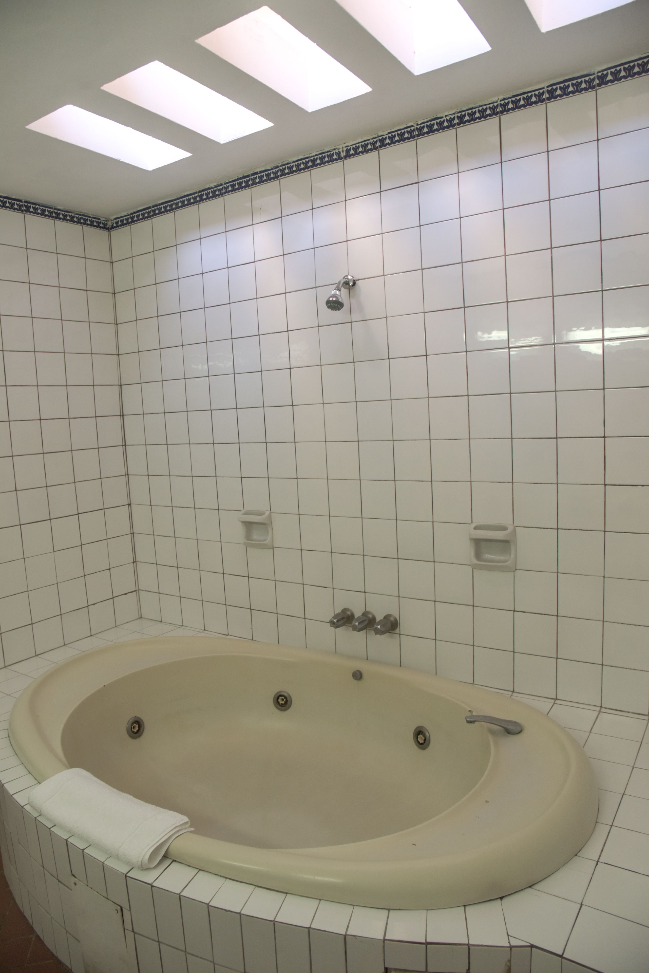 Un baño con bañera independiente, paredes de azulejos blancos y un tragaluz.