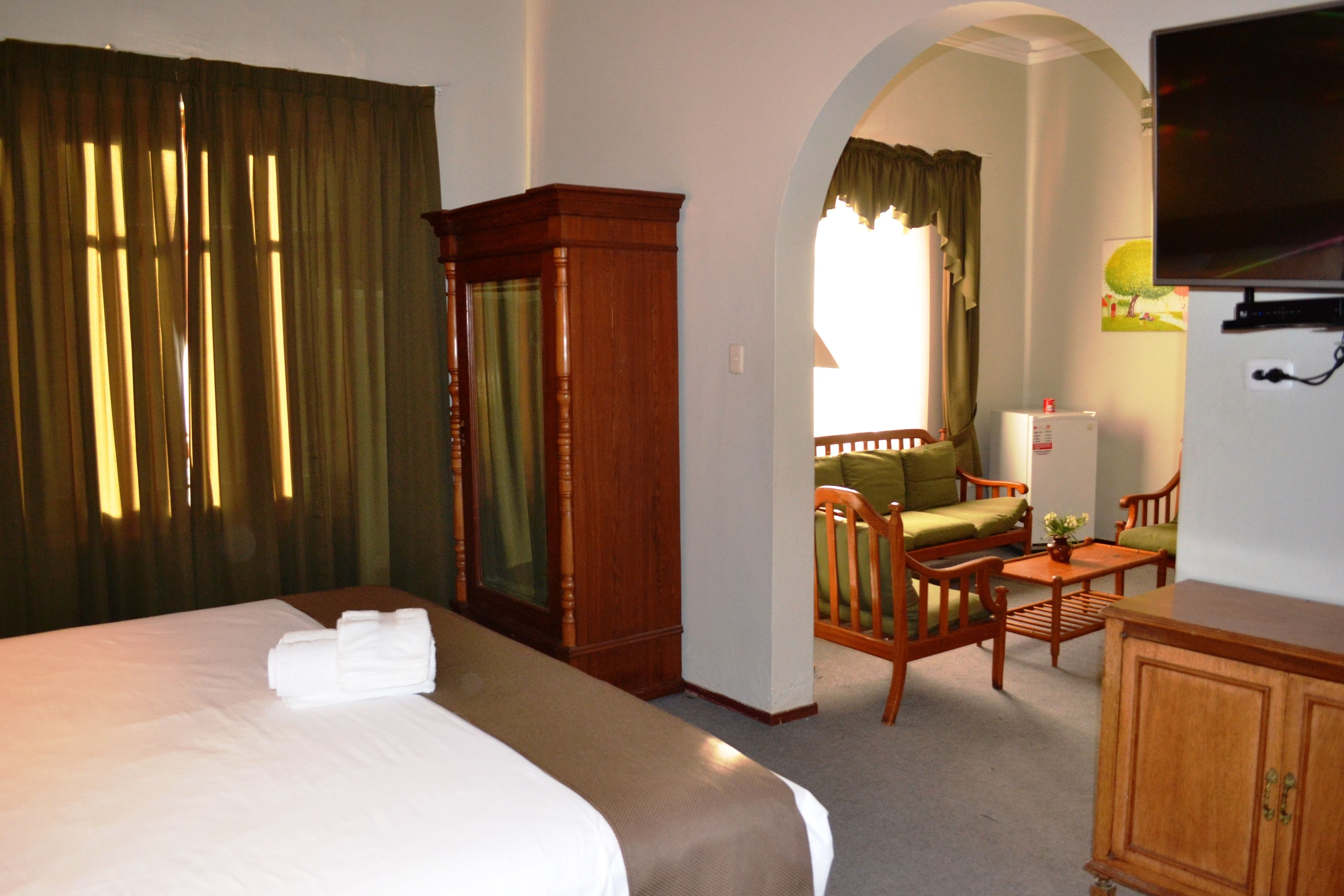 A hotel room with a large bed, a wooden wardrobe, a desk with a chair, and a television on the wall.