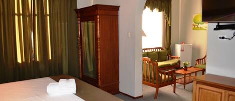 A hotel room with a large bed, a wooden wardrobe, a desk with a chair, and a television on the wall.