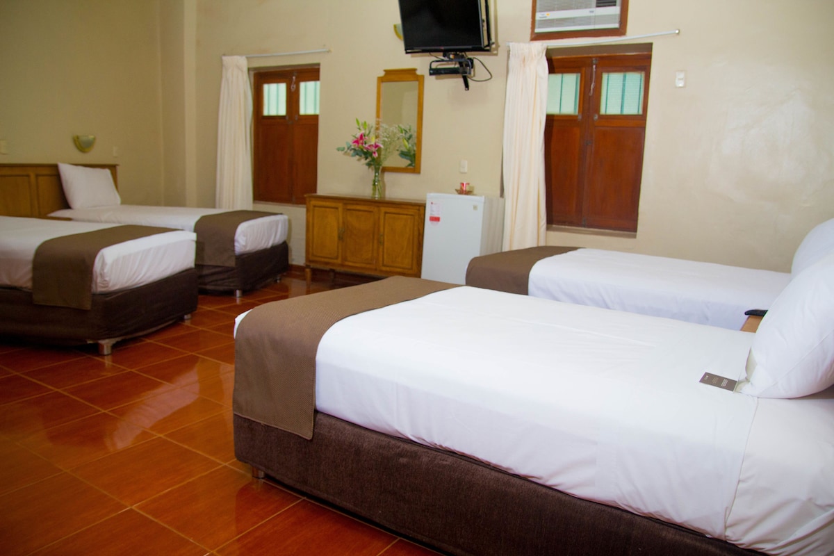A hotel room with three beds, a small cabinet, a television, and a refrigerator.
