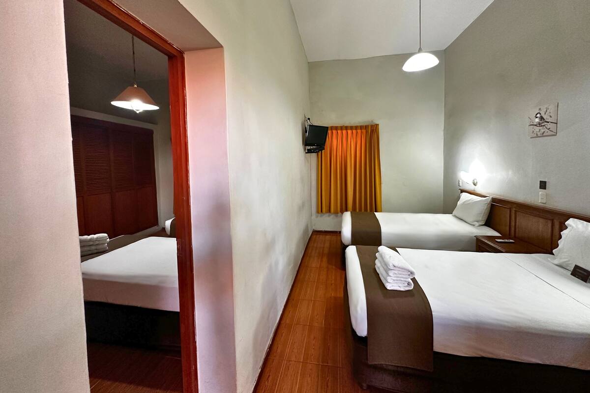 A hotel room with two beds, a TV, a wooden floor, and a window with curtains.