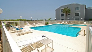 A pool area with lounge chairs and a table, surrounded by a white fence, with a building in the background. - Sea Cloisters 204c 2 Bedroom Condo by RedAwning (North Myrtle Beach)