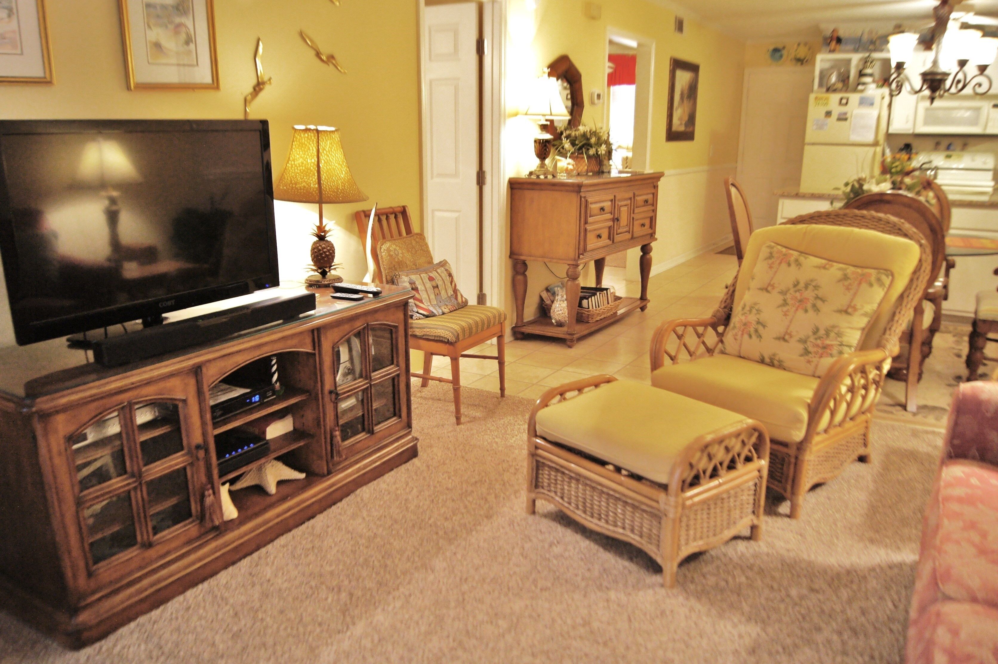 Una sala de estar con televisor, muebles de madera y una cocina al fondo.