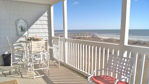A covered outdoor area with white railings, a red cushioned chair, and a table with chairs. - Sea Cloisters 204c 2 Bedroom Condo by RedAwning (North Myrtle Beach)